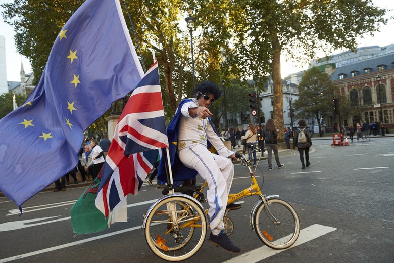 A man dressed as Elvis cycles on a tricycle with European Union, Union Jack, and Welsh flags.
